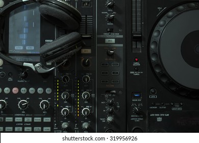Upper view closeup of dj musical mixer professional console black color with many buttons and knobs and glamour headphones with pastes in night club or studio on digital background, horizontal picture