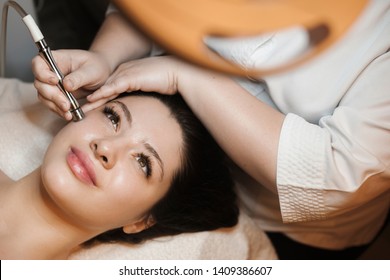 Upper view portrait of a beautiful caucasian female leaning on a bed with eyes open while having non invasive microdermabrasion on her face in a spa salon.