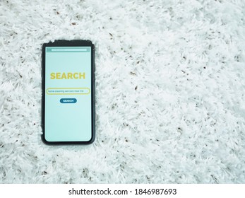 Upper view of smartphone with cleaning service search screen on carpet.