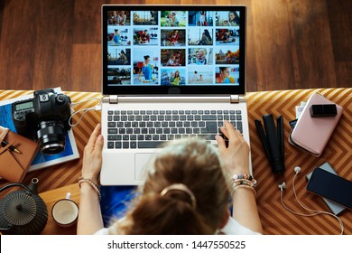 Вид сверху стильной женщины, сидящей на диване в современной гостиной, смотрит на библиотеку изображений при переносе фотографий с фотокамеры DSLR на ноутбук.
