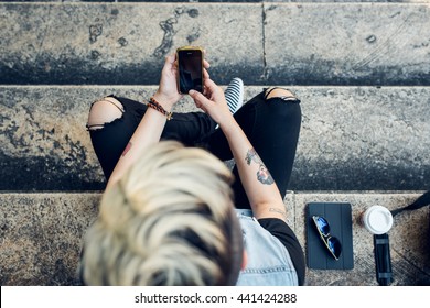 An upper view of stylish young woman using her cell phone while sitting on stairs in the city. We live in a connected world