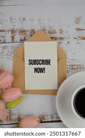 upper view of text of SUBSCRIBE NOW on a piece of card with coffee and flowers on the table. 