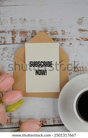 upper view of text of SUBSCRIBE NOW on a piece of card with coffee and flowers on the table. 