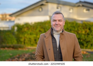 Upperbody portrait of a middle aged man in a brown coat smiling softly at the camera against an urban background