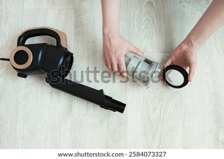Upright vacuum cleaner disassembled. Using filter for dust container in hands of Caucasian woman.