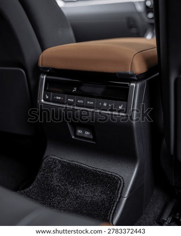 An upscale car interior featuring a brown leather center armrest and sleek console.