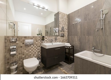 Upscale Comfortable Bathroom In European Vacation Apartment Or Hotel Suite Interior, With Upscale Accessories As Bathtub, Large Mirror, Large Sink, And Toilet Seat Incorporated Into The Wall