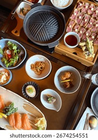 Upscale dining spread featuring artfully plated sushi and sizzling wagyu beef on a Korean hotplate, an elegant fusion of Japanese and Korean cuisine in a refined restaurant setting.
