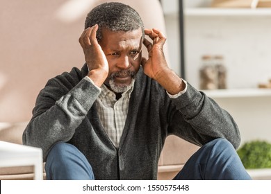 upset african american man sitting on floor and holding hands near head while suffering from migraine