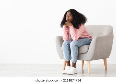 Upset African American Millennial Woman With Bushy Hair Sitting At Arm Chair At Home, Wearing Stylish Casual Outfit, Looking At Copy Space, Having Problems, Looking For Solution, Panorama