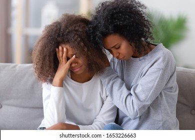 Upset african american mom sister hugging sad child teen girl consoling supporting or asking for forgiveness after fight, black mother hugging comforting depressed teenage daughter sitting on sofa