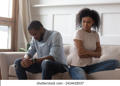 Upset african couple turn back ignore each other after fight, stubborn young black spouses sit separate on sofa not talking disappointed in bad relationship distrust jealousy in unhappy marriage