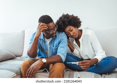 Upset african woman and man with positive pregnancy test sitting on bed at home. A sad young woman holds a pregnancy test in her hand. The concept of unwanted pregnancy