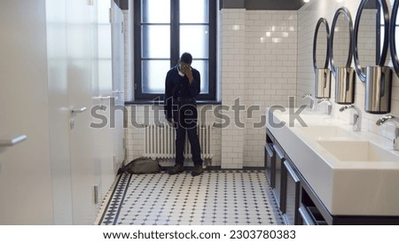 Upset African-American teen student sit on floor in school bathroom. Stressed and lonely schoolboy sitting alone in toilet feeling frustrated