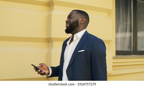 Upset Afro Businessman Receiving Bad Message On Phone. African American Man Getting Bad Letter On Smartphone At Urban Street. Sad African Guy Walking Outdoors In Slow Motion