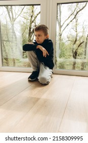 Upset, Angry Boy Of 6-7 Years Old Sits Near The Window. Portrait Of A Boy, Front View