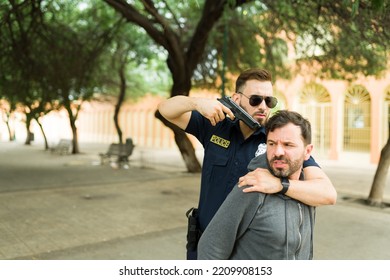 Upset Angry Cop Pointing His Gun To The Head Of A Criminal Suspect While Making An Arrest In The Street