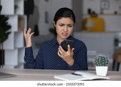 Upset annoyed Indian girl having problems with smartphone, looking at screen, feeling frustrated, angry, disappointed. Mobile phone user woman getting bad connection, spam, app work errors - Shutterstock ID 2103373391