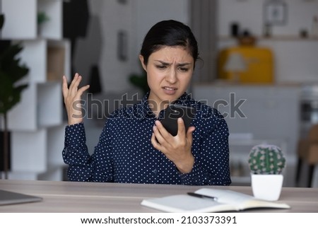 Upset annoyed Indian girl having problems with smartphone, looking at screen, feeling frustrated, angry, disappointed. Mobile phone user woman getting bad connection, spam, app work errors