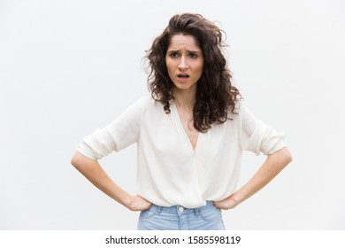 Upset annoyed woman keeping hands on hips and arguing. Wavy haired young woman in casual shirt standing isolated over white background. Conflict concept