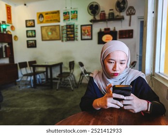 Upset Asian Female Holding Smartphone, Looking At Mobile Phone Screen With Worry While Sitting On Chair at Cafe, Anxious Muslim Woman Reading Unplesant Message, Closeup. - Powered by Shutterstock