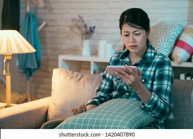 Upset Asian Korean Wife Viewing Online Content In Smart Phone Sitting On Sofa In Dark Living Room At Home At Night. Sad Girl Binge Watching Love Film Romantic Miserable Movie On Cellphone Frowning.