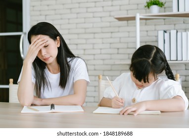 Upset Asian Mother Is Angry To Little Daughter Teach And Doing Homework Writing And Reading. Her Don't Understand While Sitting On Desk At Home. Children Education Problem, Parent And Child Conflict.