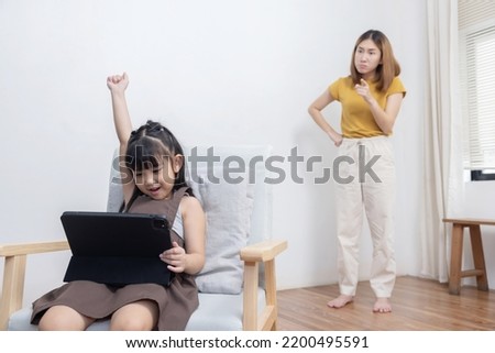 Upset Asian Mother Looking at Her Kid Playing Game on the Tablet  While Studying