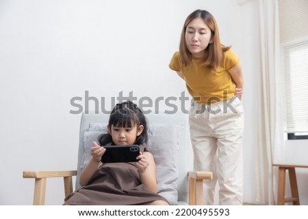 Upset Asian Mother Looking at Her Kid Playing Game on the Smartphone While Studying
