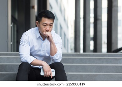Upset Asian sitting on stairs outside office center, depressed man and frustrated businessman