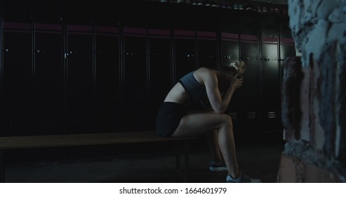 Upset athletic blonde woman sitting alone, lying down on bench in dark gym locker room tired after bad day slow motion. - Powered by Shutterstock