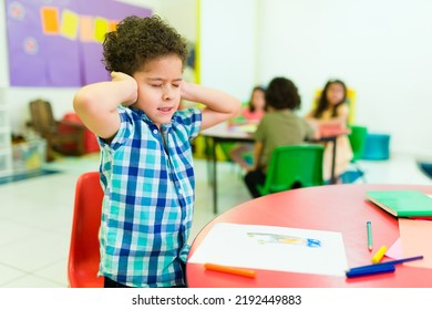 Upset autistic little boy covering his ears and feeling distressed and overwhelmed by the loud noises in preschool 
