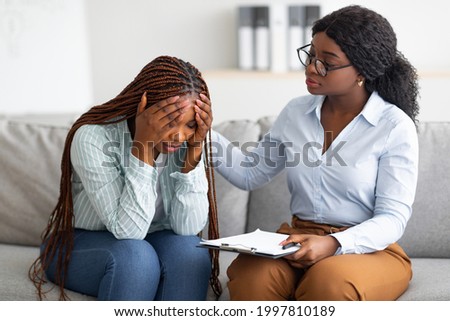 Upset black lady with nervous breakdown consulting psychologist, having session with counselor at clinic. Professional psychotherapist comforting depressed female patient at office