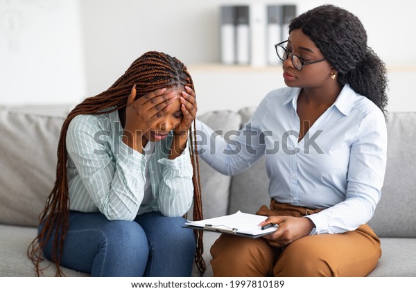 Upset black\
lady with nervous breakdown consulting psychologist, having session\
with counselor at clinic. Professional psychotherapist comforting\
depressed female patient at\
office