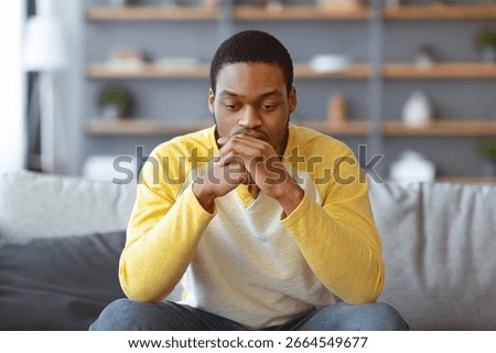Upset black man having problems, sitting on couch at home