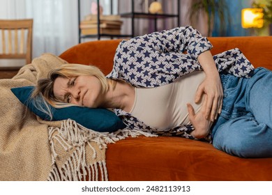 Upset blonde woman embracing belly suffering from stomachache lying on sofa. Unhappy sad Caucasian girl having menstrual painful feelings, resting on couch. Gastritis, abdominal or period pain concept - Powered by Shutterstock