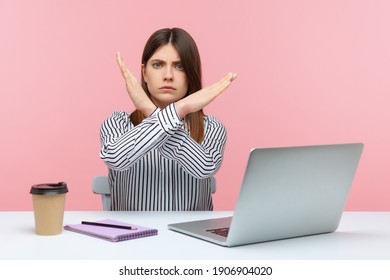 Upset bossy woman office worker sitting at workplace crossing hands showing x sign, rejecting and finishing sexual harassment at work. Indoor studio shot isolated on pink background