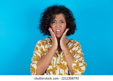 Upset Brunette Arab Woman Wearing Hawaiian Shirt Over Blue Background Touching Face With Two Hands