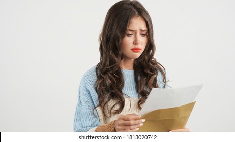 Upset Brunette Girl In Sweater Opening Envelope Sadly Looking Exam Results Over White Background. Upset Expression
