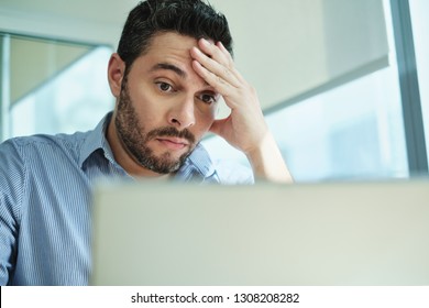 Upset Business Man Working With Laptop Computer In Office, Feeling Stressed And Anxious For Possible Data Loss. Adult Hispanic Executive Under Stress At Work For Technology Problems And Software Pc