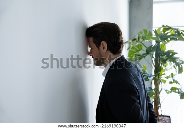 Upset businessman banging his head against wall\
in despair looks stressed having problems at work, bankruptcy,\
business failure unsuccessful negotiations, project loss, failed\
job interview concept