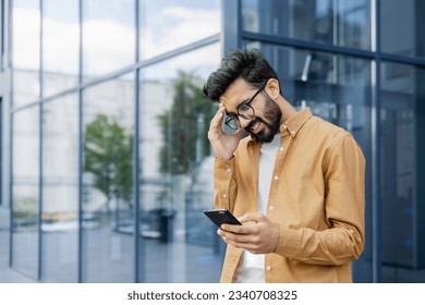 Upset businessman received message with bad news, hispanic man outside office alarm clock cheated and bankrupt, man unhappy with achievement results walking in city. - Powered by Shutterstock