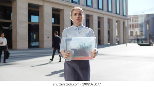 Upset Businesswoman Walking Outdoors With Box Of Stuff Leaving Business Center. Female Office Worker Lost Her Job. Portrait Of Stressed Dismissed Woman Manager Outside Office Building