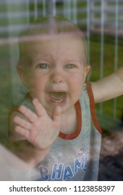 Upset Caucasian Toddler Baby Boy Cries Through Glass Window From Separation Anxiety Worries Woes At Daycare While Parent Leaves