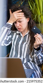 Upset confused online buyer woman holding credit card, looking at laptop computer screen,sit at home in striped shirt.Debt problems, insecure online payment,failed transaction, loss of money.Vertical