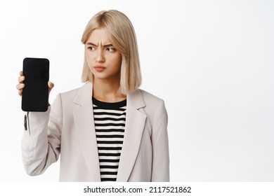 Upset Corporate Woman, Showing Mobile Phone Screen, Smartphone Display, Frowning And Looking Concerned, Express Dislike, Standing Over White Background