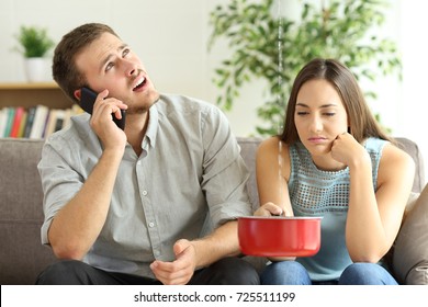 Upset couple sitting in a couch in the living room and calling insurance for home leaks 
