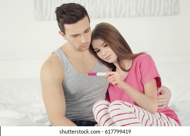 Upset Couple Sitting On Bed And Looking At Pregnancy Test