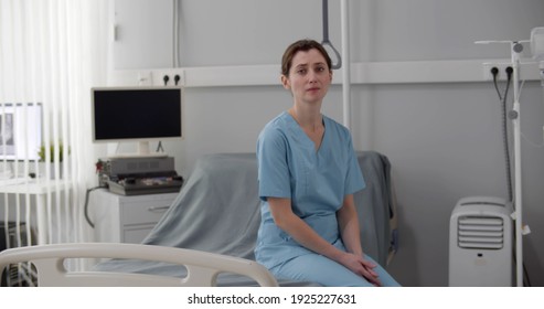 Upset Crying Female Nurse Sitting On Empty Hospital Bed. Portrait Of Frustrated And Stressed Woman Doctor Sitting In Hospital Ward And Crying Feeling Sad And Depressed