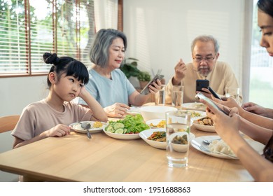 Upset Daughter Sitting At Lunch Table Looking To Addicted Parents And Grandparents Using Smartphones While Eating Breakfast. Ignoring Family Not Paying Attention On Small Child. Bad Parenting In House